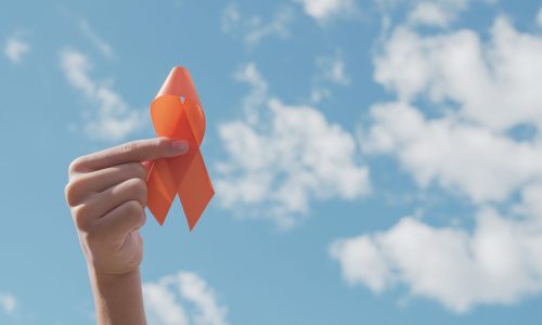 hands-holding-orange-ribbon-over-blue-sky-min